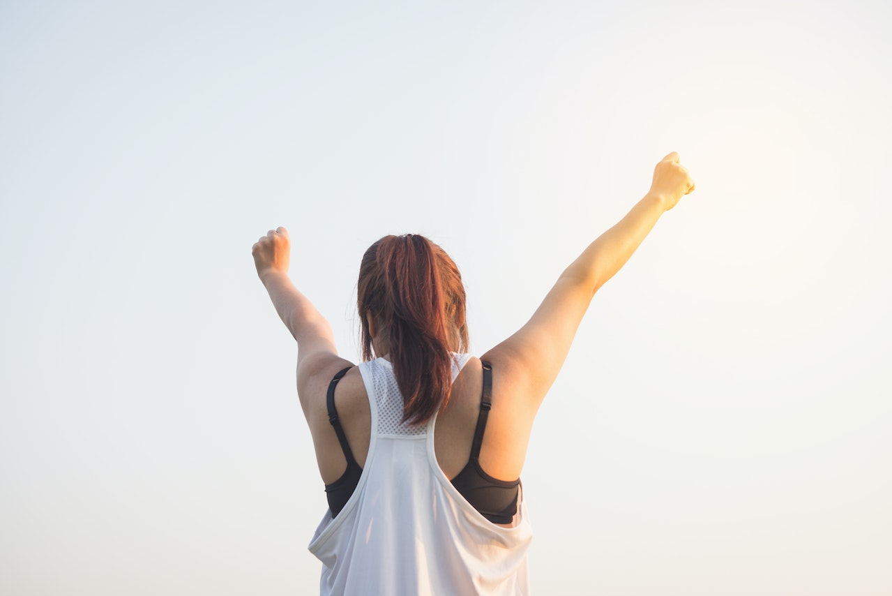 woman, photographed from behind, holding fists triumphantly in the air